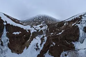 Wide angle drone view of snowy mountains under cloudy gloomy sky in Iceland