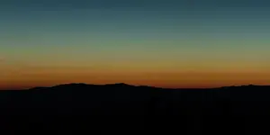 Wide angle panorama silhouette mountain tops in orange blue gradient sunset