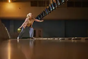 Throwing Prints: Wide angle side view at senior woman playing bowling alone while enjoying active entertainment at bowling alley