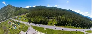 A wide banner aerial view of the direct road with cars in the Altai mountains surrounded by green forest and trees