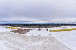 Wide winter aerial view over snowy fields with trees and a cloudy horizon, shot by a drone