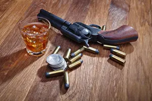 Liquor Prints: Wild west revolver and ammunitions with glass of whisky and ice with old silver dollar on wooden bar table