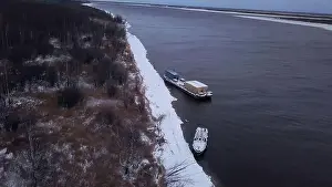 Winter frozen river. Clip.Cargo boats and bare trees on the shore taken from a bird's-eye view. High quality 4k footage