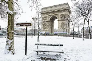 Snowfall Prints: Winter in Paris in the snow. The Arc de Triomphe with a public bench covered in snow in the foreground