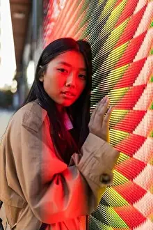 Concentrate Prints: Wistful ethnic female in casual clothes with long hair looking at camera while leaning on wall with neon illumination