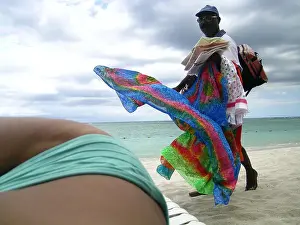 Woman in bikini sunbathing at beach as beach hawker passes by, Mauritius