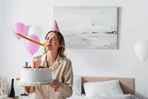 Pajama Prints: Woman blowing party horn and holding birthday cake on bed