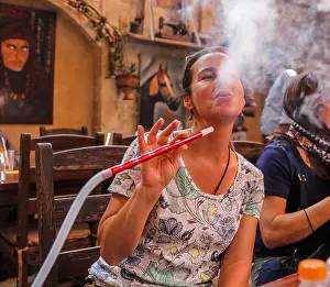 Tobacco Prints: A woman blows smoke from her hookah pipe inside a restaurant in Amman, Jordan