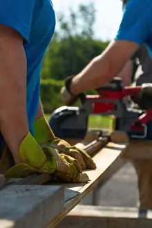 Rebar Prints: A woman in a blue shirt holds down a piece of rebar while another worker uses a cordless band saw to cut through it