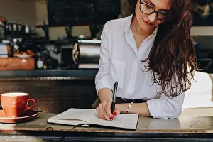 Casuals Prints: Woman in the cafe writing notes in a book while sitting at coffee shop