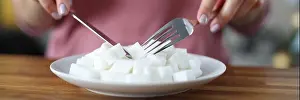 Carbohydrates Prints: Woman eating lumps of sugar from plate with knife and fork at table close-up