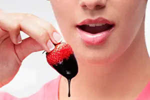 One Young Woman Only Prints: Woman eating a strawberry dipped in chocolate sauce