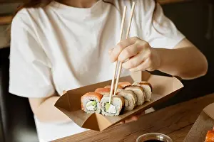 Unwind Prints: Woman enjoying a selection of sushi rolls using chopsticks