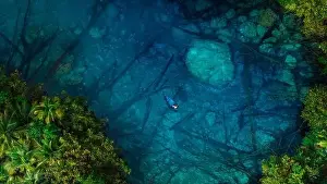 Woman floating on boat in transparent lake with crystal blue water in Indonesia. Aerial view