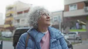 Pensive Prints: Woman with grey hair wearing a blue jacket looks up inquisitively on a city street