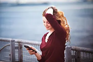 Blond Hair Prints: Woman with hand in hair using smart phone against river
