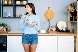Beautiful Woman Prints: Woman having food while leaning on kitchen counter