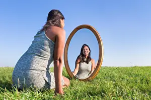 Kneeling Prints: Woman kneeling on grass looking at mirror image