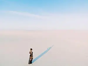Woman in lace black dress walks in desert and casts a shadow on white sand. View from drone