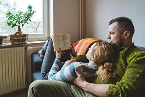 Mid Adults Prints: Woman lying on man's lap and reading book at home