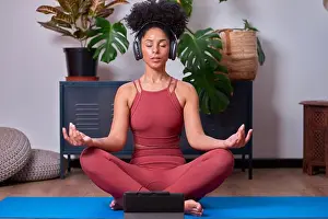 Mindfulness Prints: Woman Meditating in Yoga Pose with Headphones at Home Studio on a Blue Mat