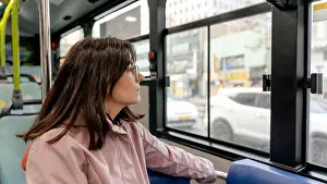 Pensive Prints: A woman in a pink coat looks out the window of a bus navigating the bustling streets of Seoul
