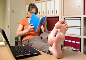 Shoeless Prints: Woman reading home office with bare feet on desk