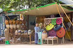 Headwear Prints: Woman selling traditional conical hats and parasols on stall at Mingun