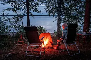 Campsite Prints: Woman sitting by the campfire in the forest on the banks of Lake Siljan in Dalarna, Sweden