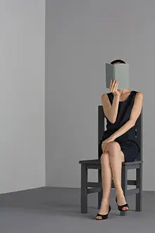 Empty Space Prints: Woman sitting in chair, holding open book in front of face