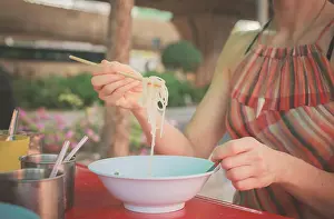 Noodles Prints: A woman is sitting at a table in the street and is eating noodles