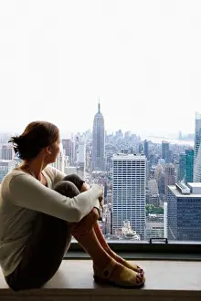Sideview Prints: Woman sitting on a window sill while looking at Empire State Building