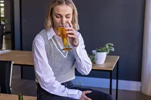 Curtains Prints: Woman sitting on wooden desk sipping amber beverage in home office with green bottle