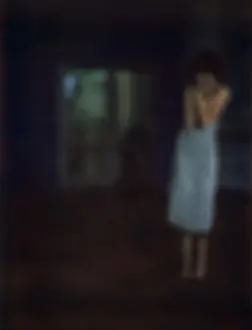 Suffering Prints: Woman standing in dark room with arms against chest, defocused