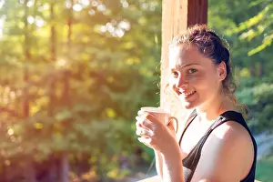 Wooden House Prints: Woman standing on porch of house in morning wooden cabin cottage drinking coffee or tea with sunrise light