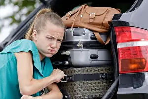 25 29 Years Prints: woman struggling to fix luggage in a car