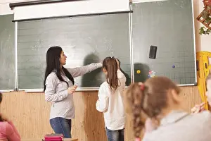 Schoolchild Prints: Woman teacher helping pupil to solve math example at the blackboard