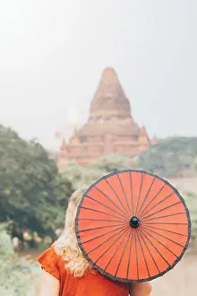 Bagan Prints: Woman with traditional Burmese red umbrella overlooking pagoda and temple of ancient Bagan in Myanmar
