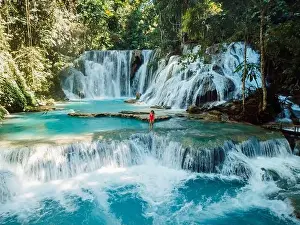 Woman walking on scenic cascade waterfalls with blue water in Central Sulawesi, drone view