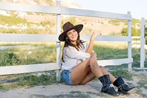 Cowboy Hat Prints: Woman wearing a cowboy hat and blue shorts is sitting on the ground
