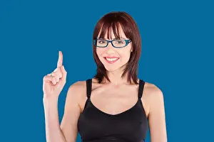 Redhead Prints: Woman wearing a tank top and blue eyeglasses with index finger pointing up on a blue background