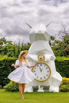 Wonderland Prints: Woman in white dress poses near giant geometric rabbit clock in garden