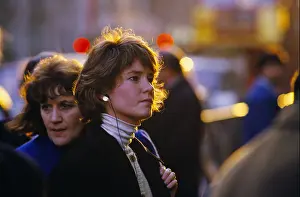 City Lights Prints: A WOMAN IN A WHITE POLO NECK AND SMALL SILVER HAMMERED EARINGS USES EARPHONES IN STREET IN LONDON