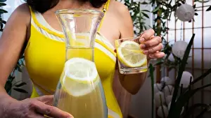 Bikini Prints: Woman in a yellow summer top outfit with a water bottle offers a water glass with a juicy lemon slice