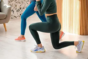 Quadriceps Prints: Two women in athletic wear perform lunges as part of their indoor fitness routine