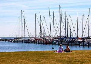 Appreciating Prints: Two women sit and admire moored yachts at Dragør fishing village near Copenhagen in Denmark with wind farm