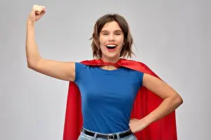 Superhero Prints: women's power and people concept - happy woman in red superhero cape showing arm bicep muscle over grey background