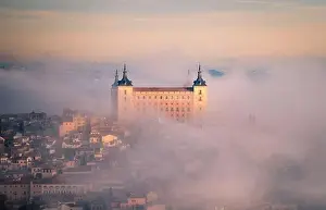 Toledo Prints: From above wonderful landscape of medieval castle built over city in misty colorful sunrise surrounded by clouds