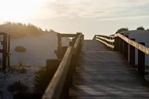Golden Light Prints: A wooden boardwalk between the sand dunes towards the sea at a beautiful sunset