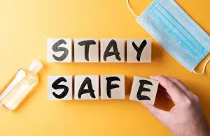 Social Distancing Prints: words STAY SAFE on wooden blocks on orange background with protective face mask and hand sanitizer